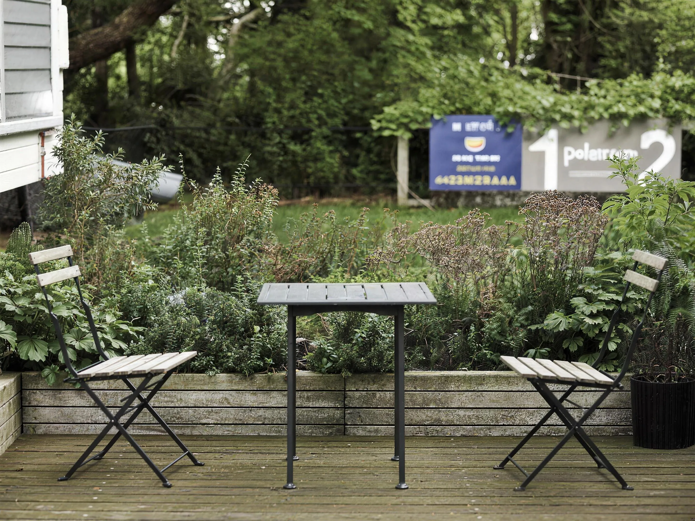Terrastuin met zithoek — Nederlandse achtertuin met een houten terras, zithoek en verzorgde border eromheen, gewoon daglicht.