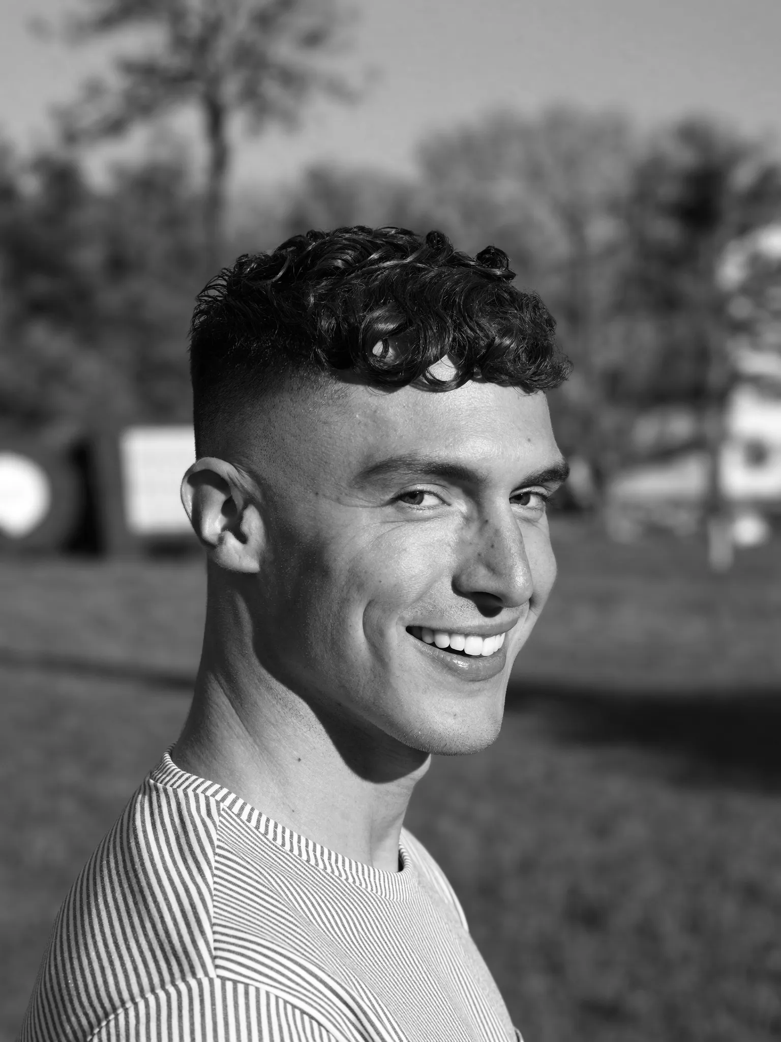 Krullen — Zwart-witportret van een man met een getextureerde krullenkop, kort opgeschoren aan de zijkanten. Onscherpe achtergrond van een Nederlands park.